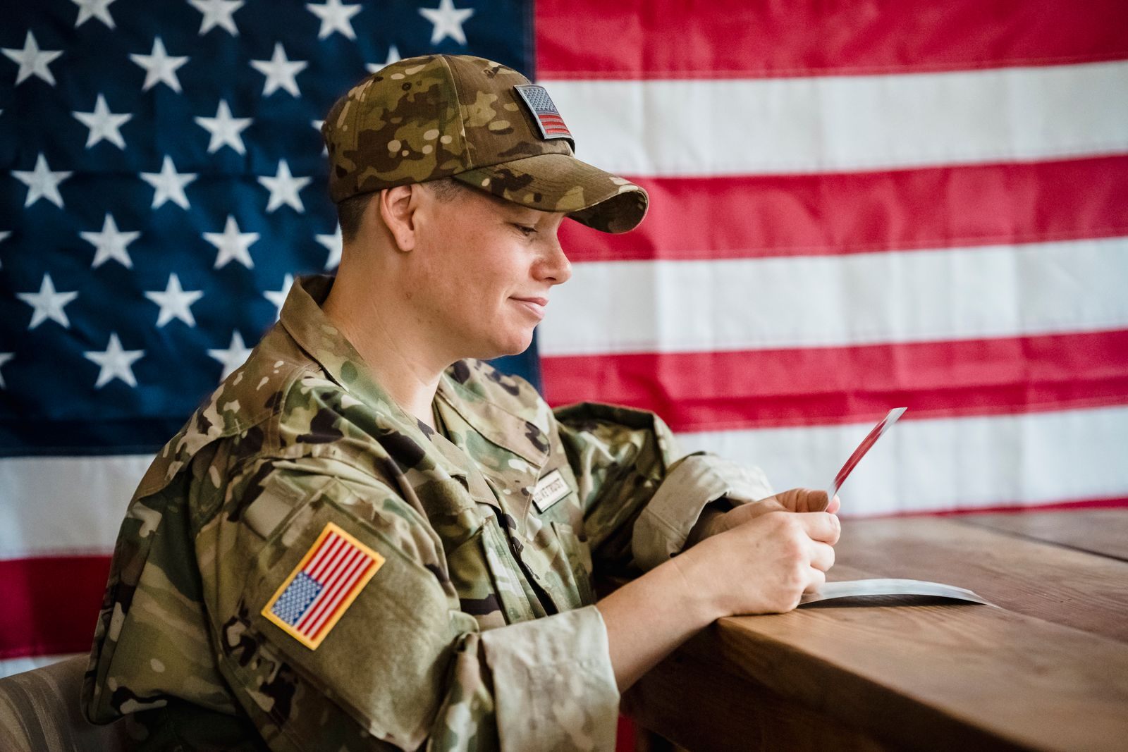 Service member in camouflage uniform at a desk in front of an American flag