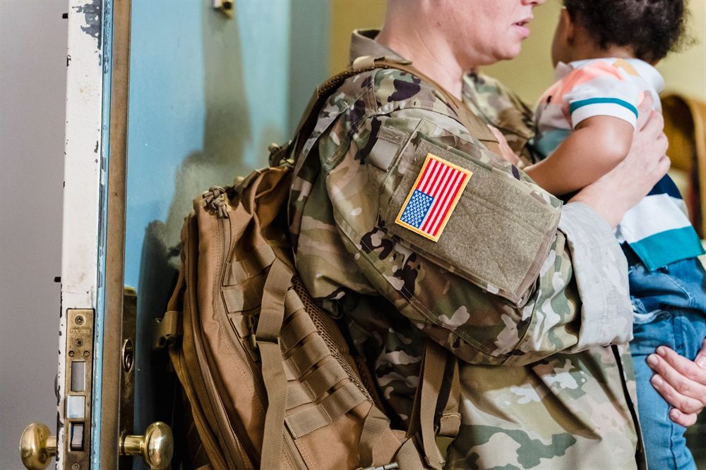 Service member in uniform holding a young child at home