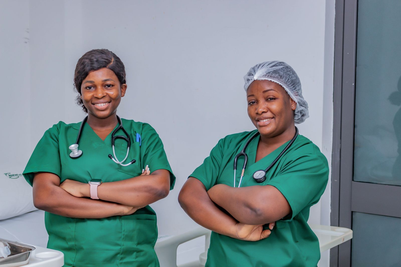 Two smiling nurses in green scrubs with stethoscopes